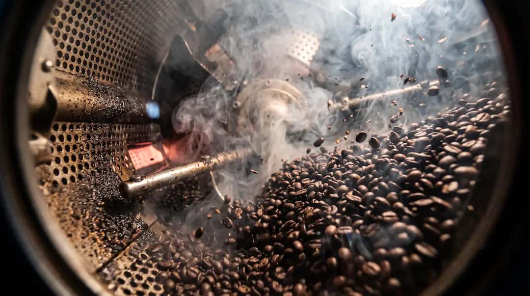 Grãos de café sendo torrados, com fumaça saindo do torrador